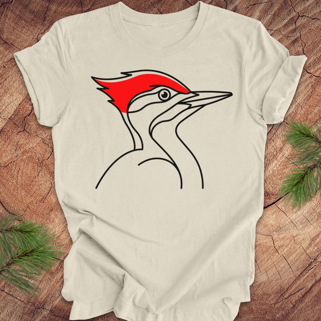 An off-white t-shirt laid flat on a rustic wood background, featuring a minimalist line art graphic of a woodpecker with a bright red crest.
