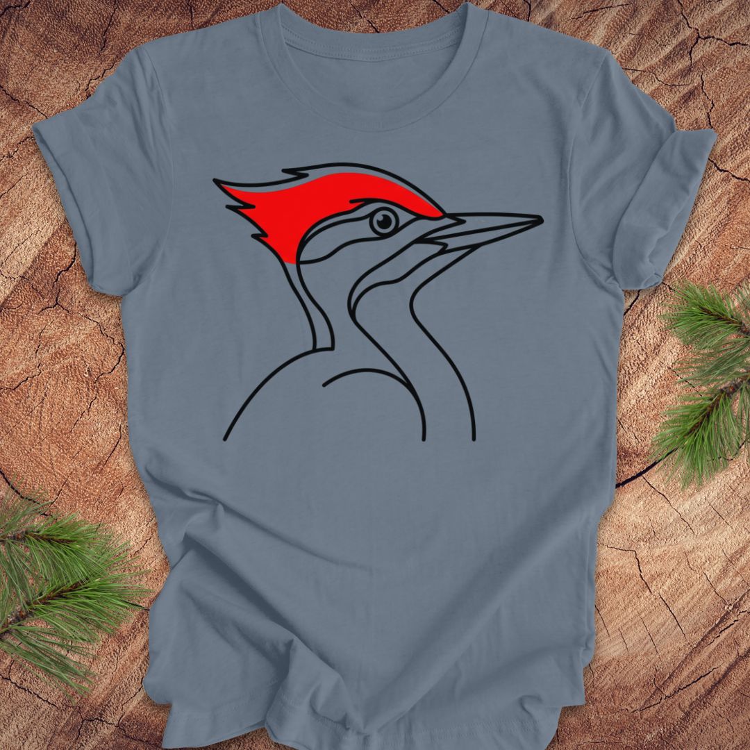 A slate blue crewneck t-shirt featuring a graphic of a woodpecker with a bright red crest, laid flat on a rustic wood background with pine needles.