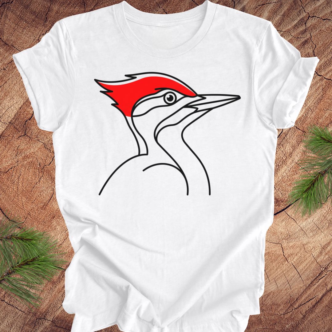 A white short-sleeve crewneck t-shirt featuring a minimalist line art graphic of a red crested bird on the chest, laid flat on a rustic wood background with pine needles in the corners.