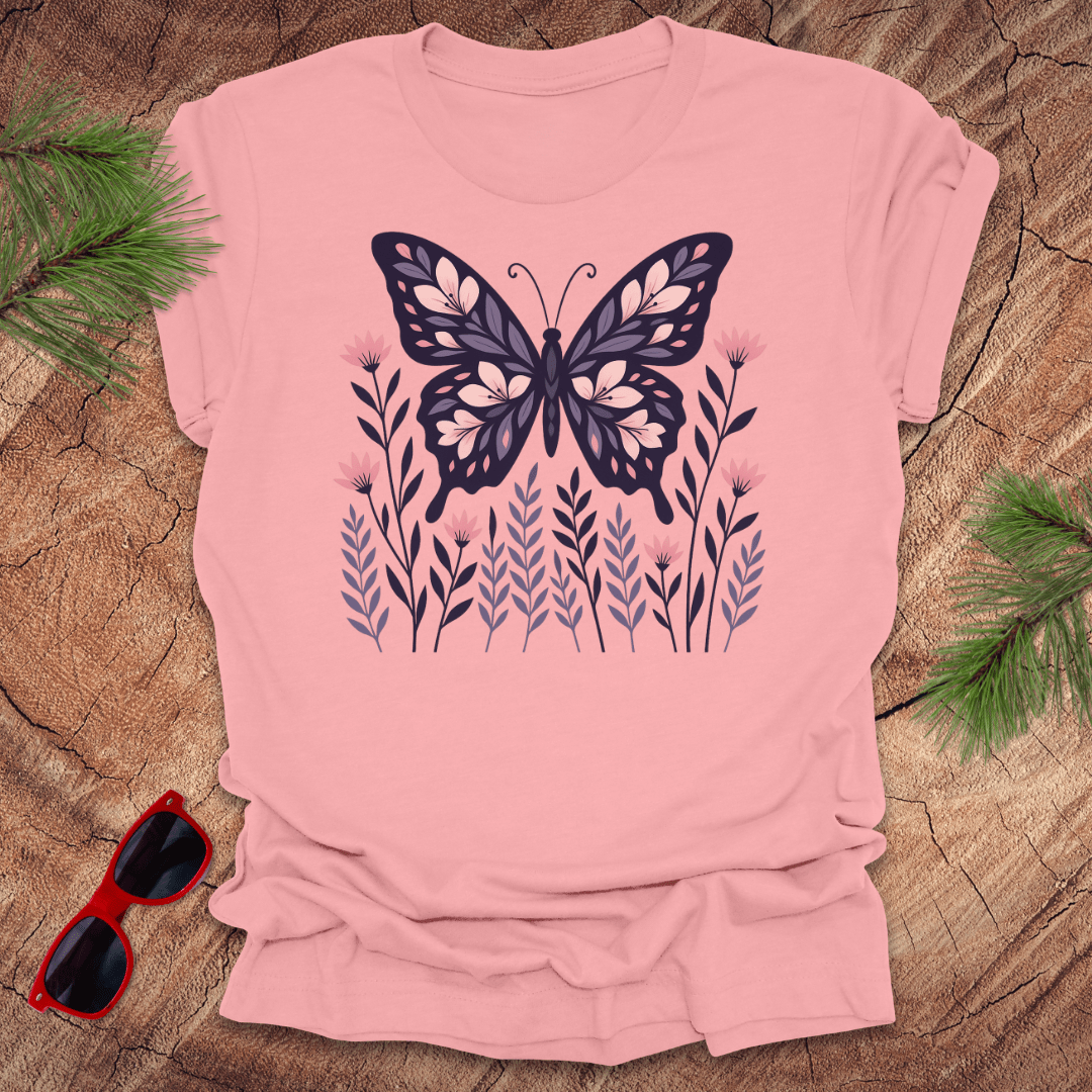 Pink t-shirt with a butterfly and flower design on a wooden surface with sunglasses and leaves.
