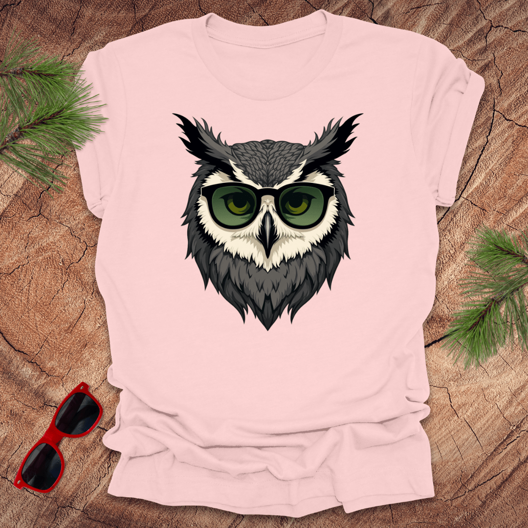 Pink tshirt with a graphic of an owl head with sunglasses on. it is on a wood background.