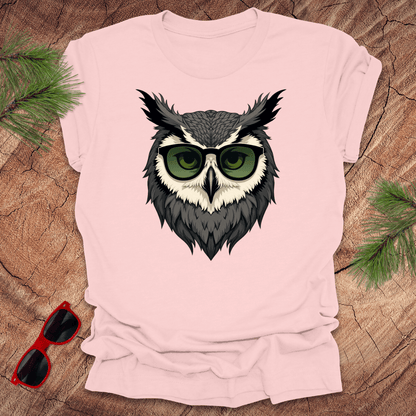 Pink tshirt with a graphic of an owl head with sunglasses on. it is on a wood background.