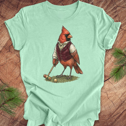 Light green t-shirt with a cardinal playing croquet design on a wooden surface.