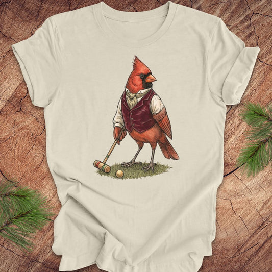 Beige t-shirt with a cardinal playing croquet illustration on a wooden surface.