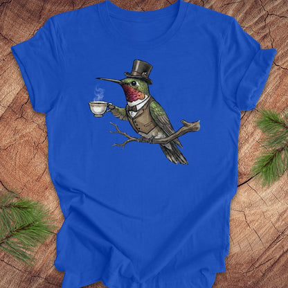Blue t-shirt with a hummingbird in a top hat holding a tea cup on a wooden surface.