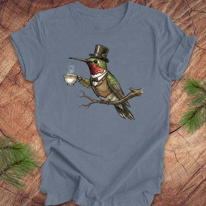 Blue t-shirt with a cartoon hummingbird wearing a top hat and holding a cup on a wooden surface.