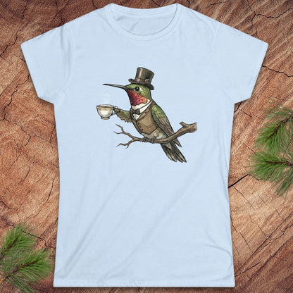 Light blue t-shirt with a design of a hummingbird in a top hat holding a cup on a wooden surface.