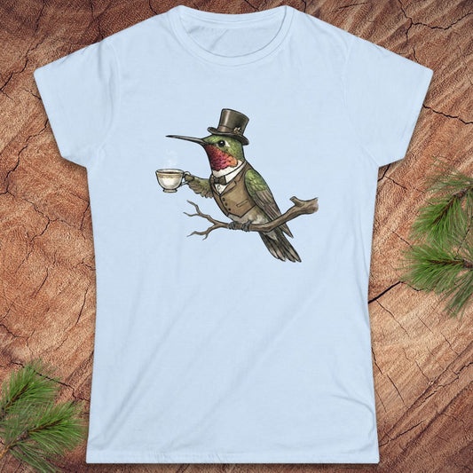 Light blue t-shirt with a design of a hummingbird in a top hat holding a cup on a wooden surface.