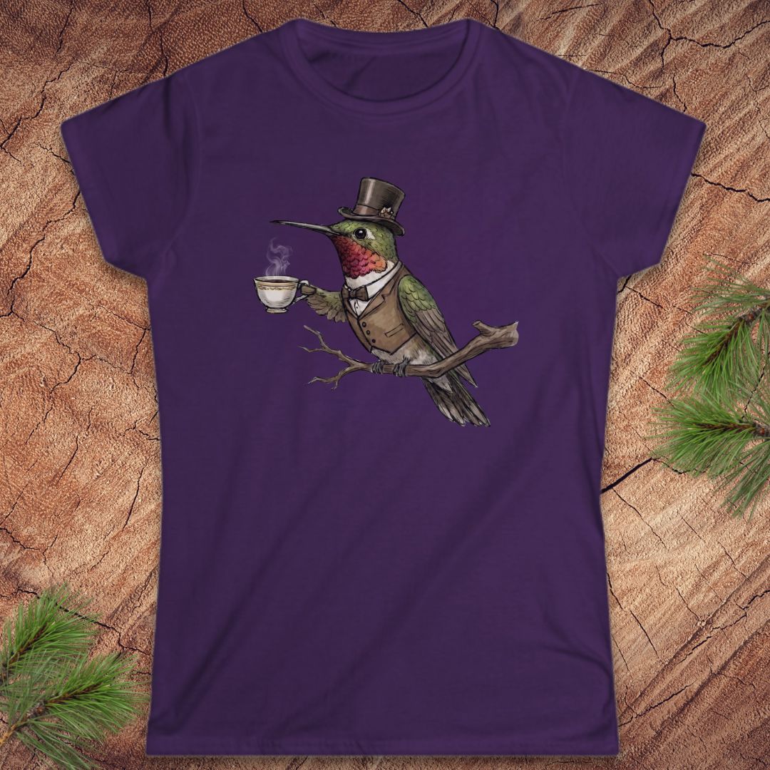 Purple t-shirt with a cartoon hummingbird wearing a top hat and holding a cup on a wooden surface.