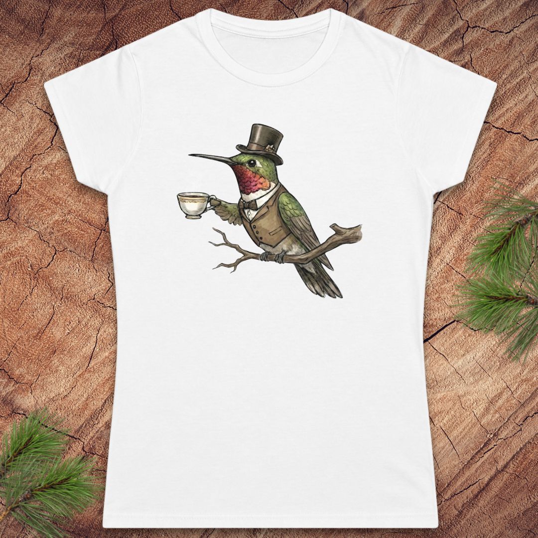 White t-shirt with a design of a hummingbird in a top hat holding a cup on a wooden surface.