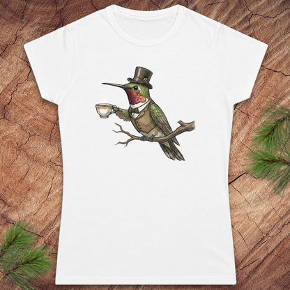 White t-shirt with a design of a hummingbird in a top hat holding a cup on a wooden surface.