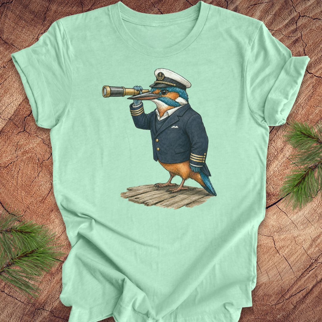 Mint green t-shirt with a kingfisher bird in a captain's outfit and spyglass on a wooden surface.