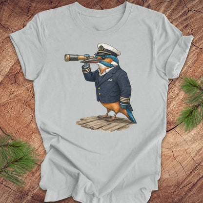 Gray t-shirt with a kingfisher bird in a captain's outfit and spyglass on a wooden surface.