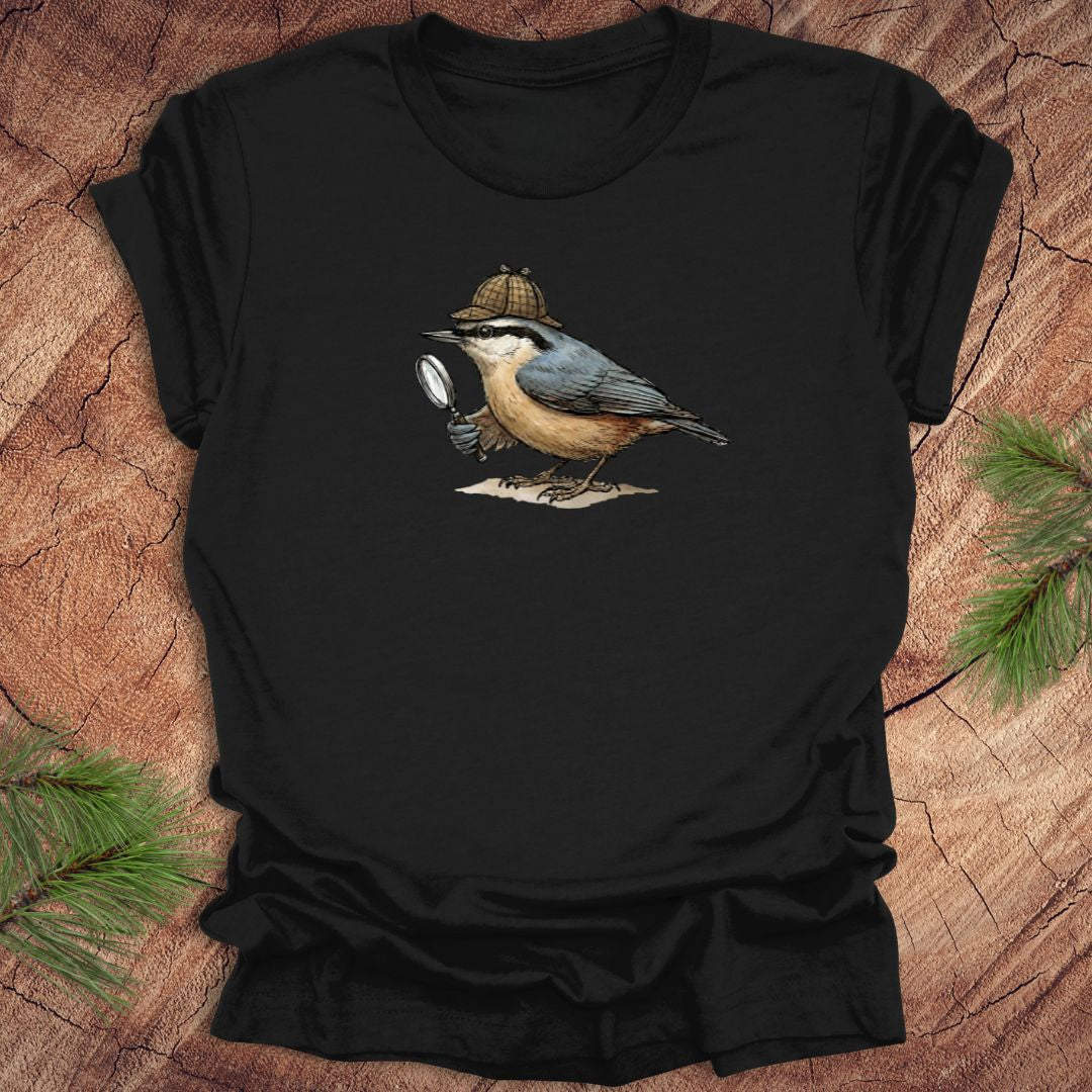 Black t-shirt with a nuthatch bird wearing a sherlock holmes cap and holding a magnifying glass on a wooden surface