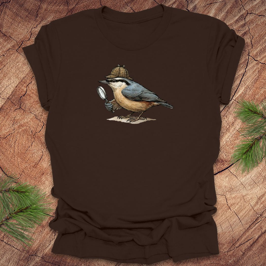 Brown t-shirt with a nuthatch bird wearing a sherlock holmes cap and holding a magnifying glass on a wooden surface