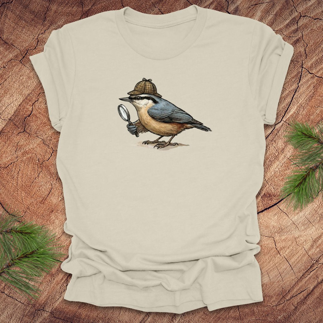 Beige t-shirt with a nuthatch bird wearing a sherlock holmes cap and holding a magnifying glass on a wooden surface