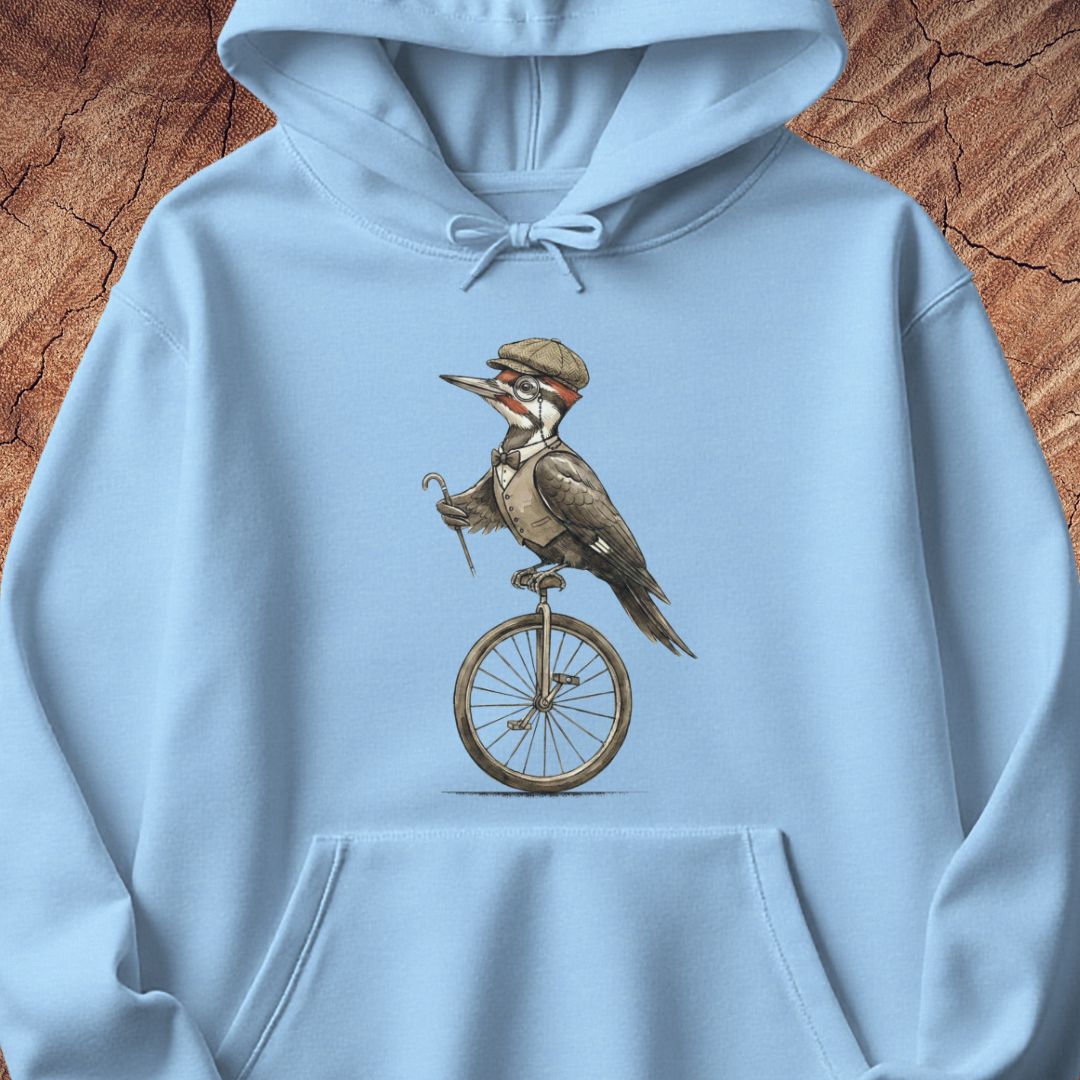 A light blue pullover hoodie featuring a vintage-style graphic of a woodpecker wearing a hat and riding a unicycle, displayed against a textured brown wood background.