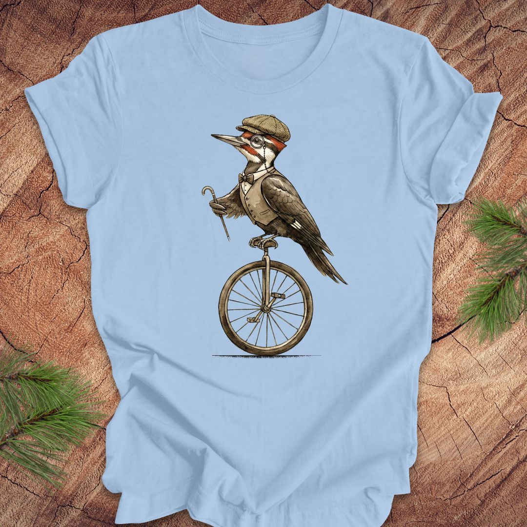 Light blue t-shirt with a woodpecker character riding a unicycle on a wooden surface.