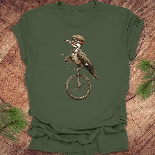 Green t-shirt with a pileated woodpecker on a unicycle graphic on a wooden surface.