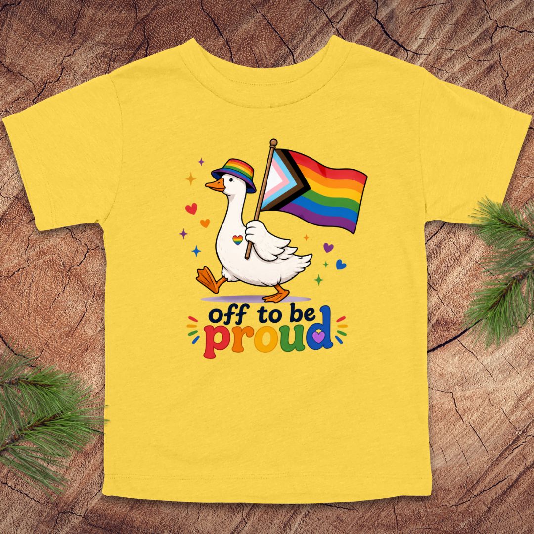 Yellow t-shirt with a duck holding a rainbow flag and 'off to be proud' text on a wooden surface.