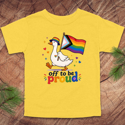 Yellow t-shirt with a duck holding a rainbow flag and 'off to be proud' text on a wooden surface.