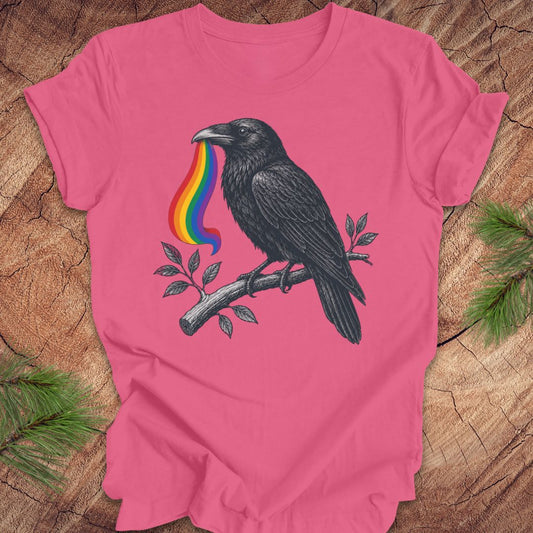 Pink t-shirt with a black crow and rainbow design on a wooden surface.