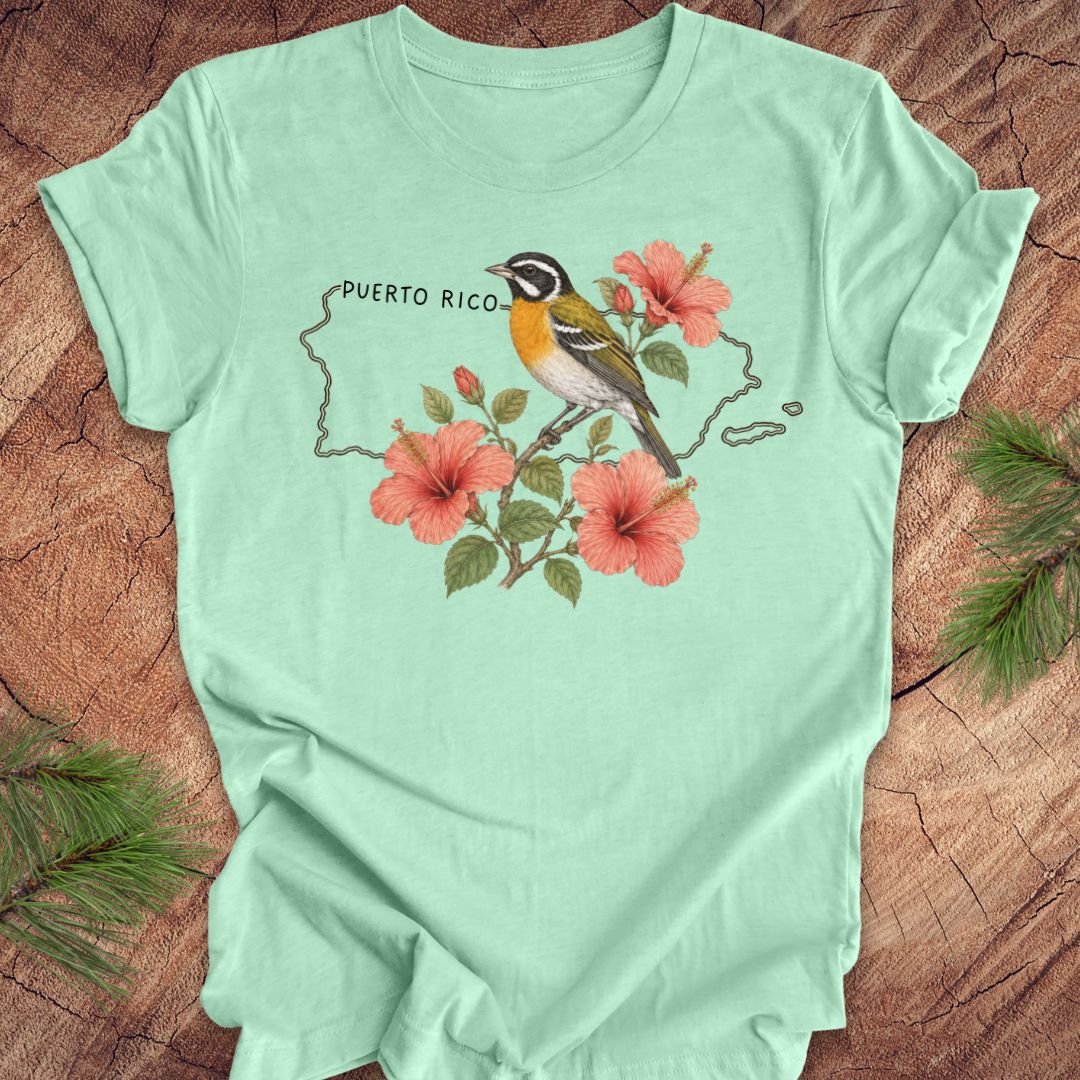 Mint green t-shirt with Puerto Rico outline and spindalis and hibiscus design on a wooden surface