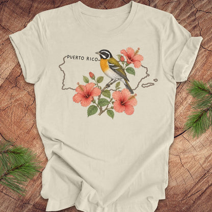 Beige t-shirt with Puerto Rico outline and spindalis and hibiscus design on a wooden surface