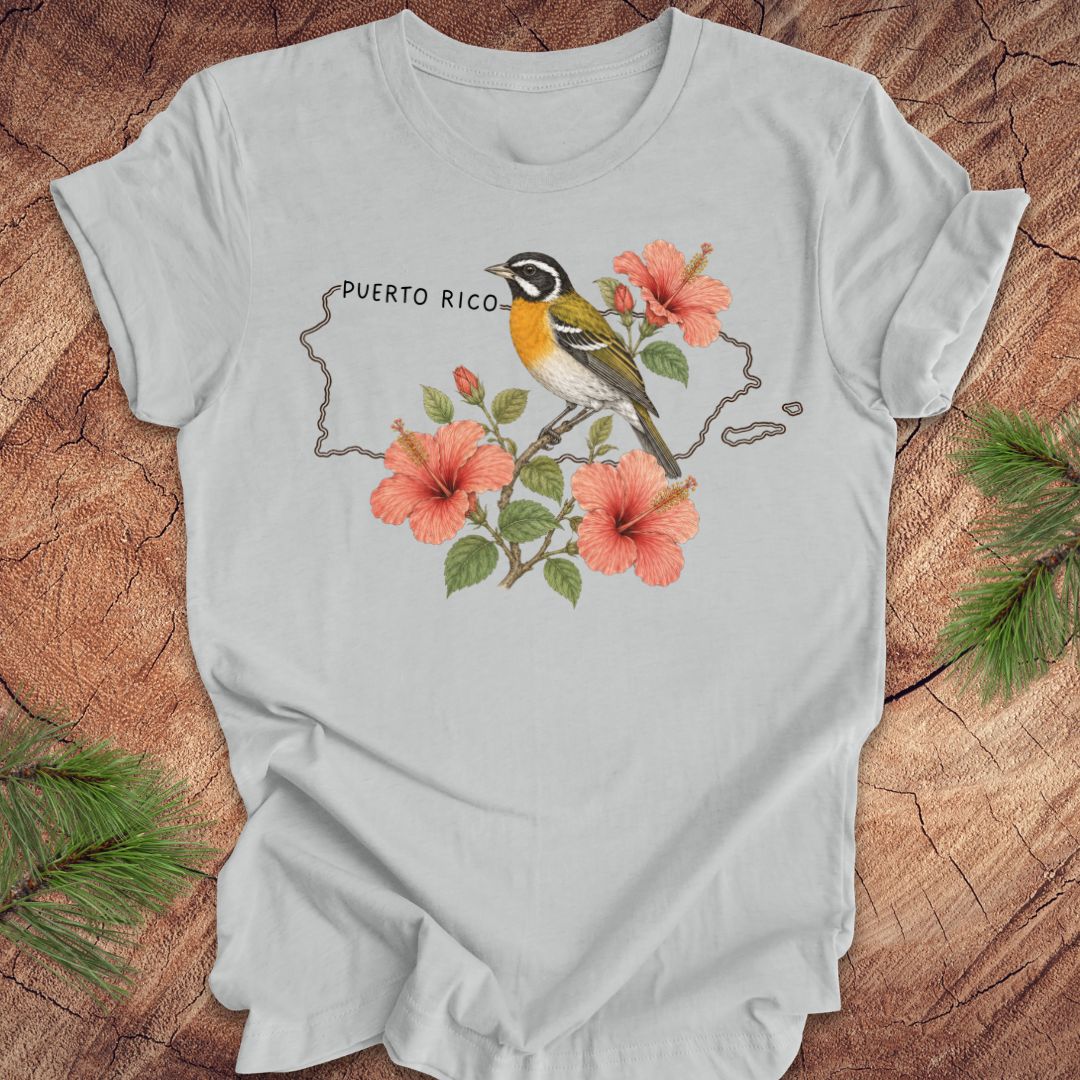 Gray t-shirt with Puerto Rico outline and spindalis and hibiscus design on a wooden surface