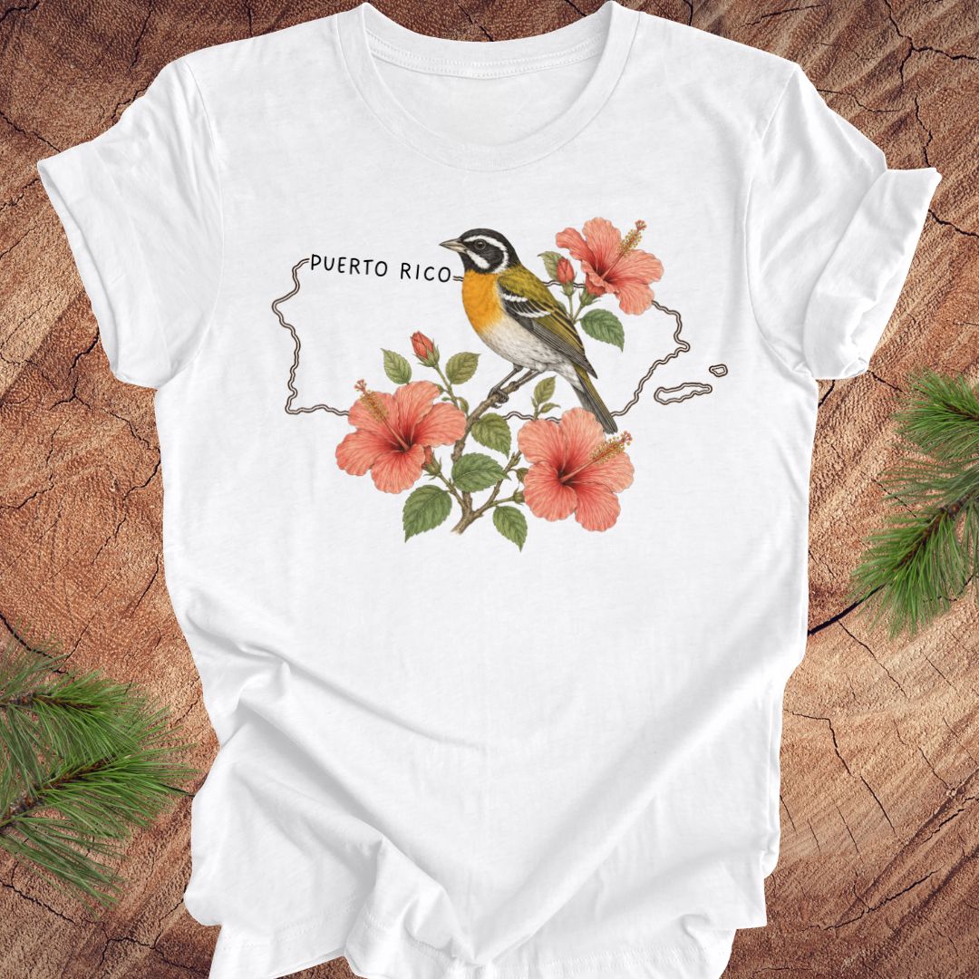 White t-shirt with Puerto Rico outline and spindalis and hibiscus design on a wooden surface