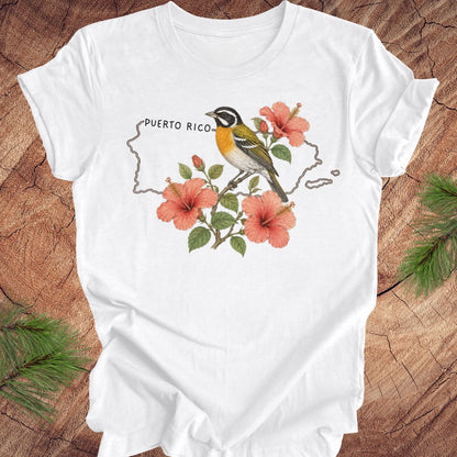 White t-shirt with Puerto Rico outline and spindalis and hibiscus design on a wooden surface