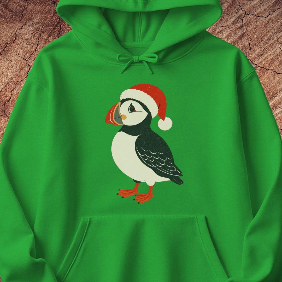 A bright green pullover hoodie featuring a cartoon puffin wearing a red Santa hat printed on the chest, laid flat on a textured brown wood background.