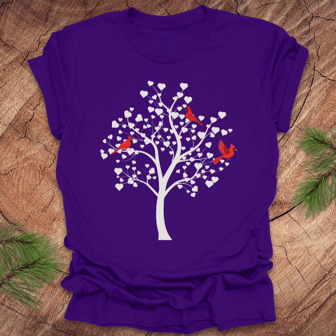 Purple t-shirt with a tree design featuring cardinals and white hearts on a wooden surface.