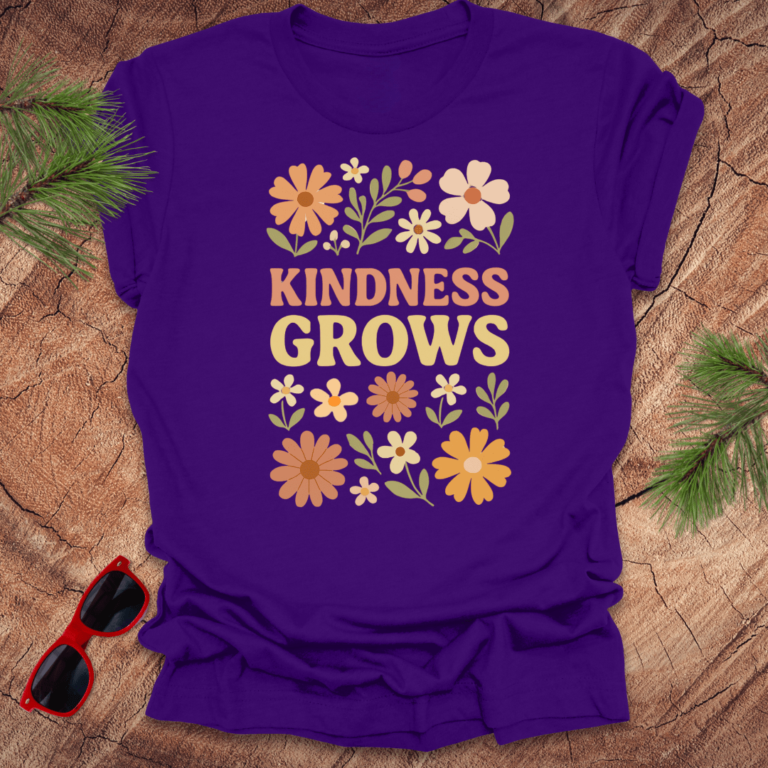 Purple t-shirt with flowers and text 'Kindness Grows' on a wood background.