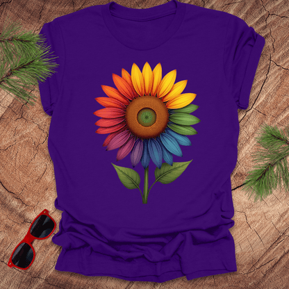 Purple tshirt with a bold rainbow sunflower graphic on a wood background.