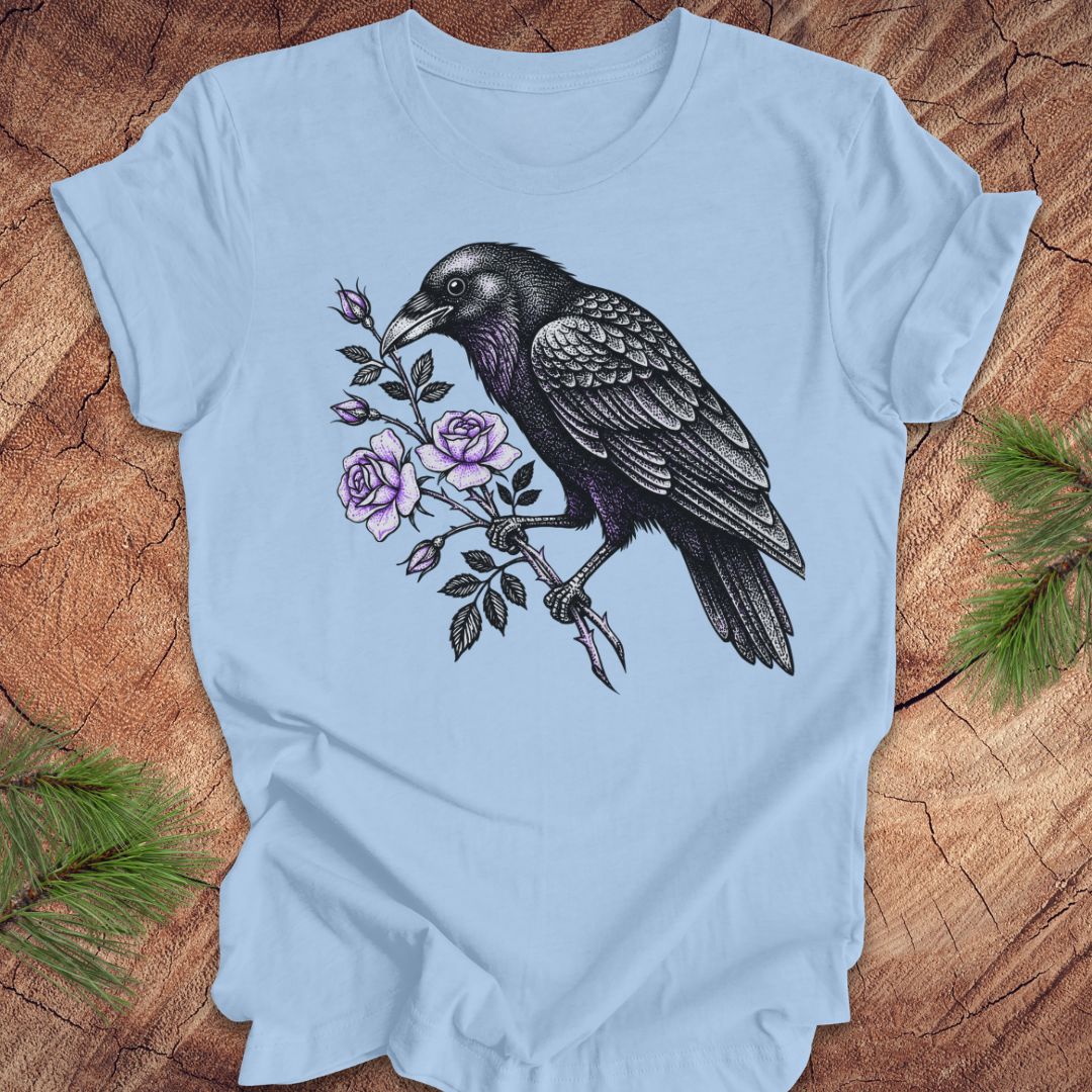 Blue t-shirt with a raven and floral design on a wooden surface