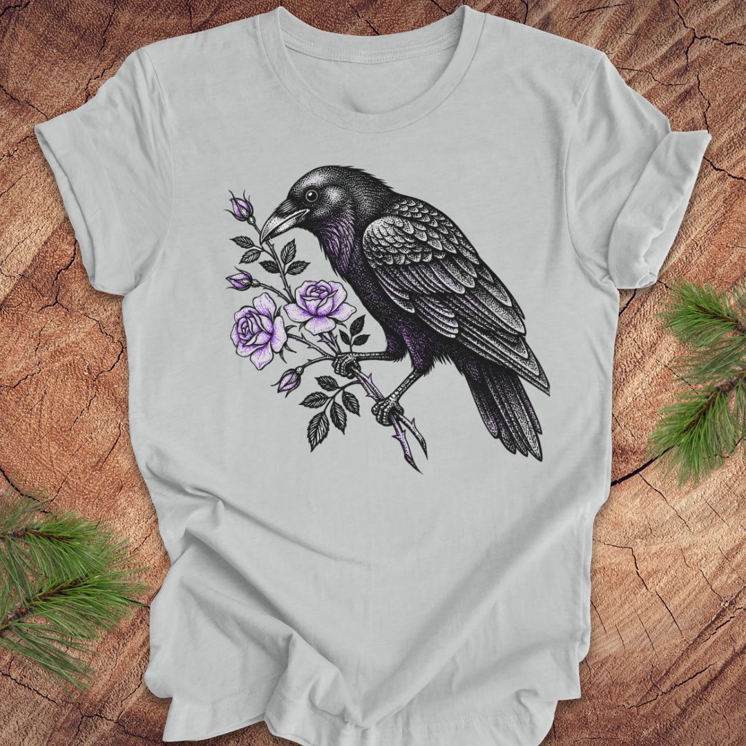 Gray t-shirt with a raven and floral design on a wooden surface