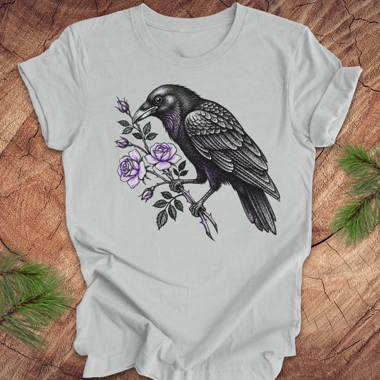 Gray t-shirt with a raven and floral design on a wooden surface