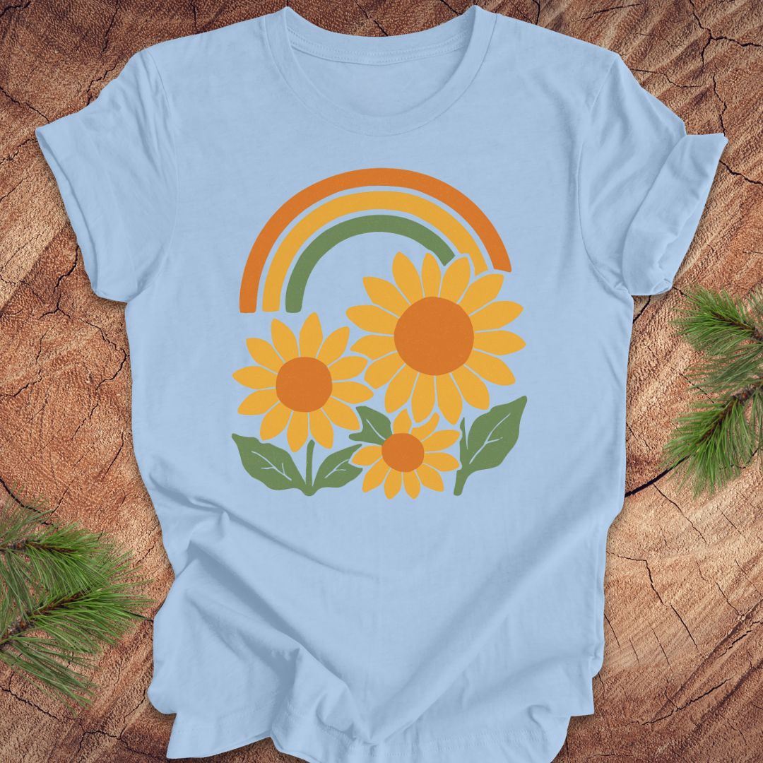 Light blue t-shirt with a rainbow and sunflower design on a wooden surface.