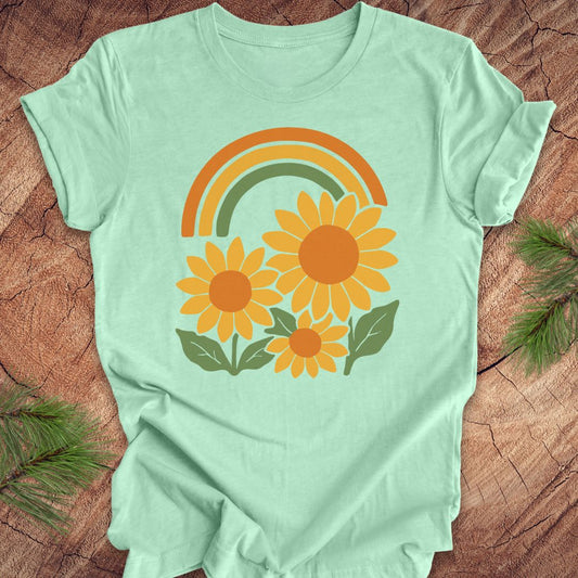 Light green t-shirt with a rainbow and sunflower design on a wooden surface.