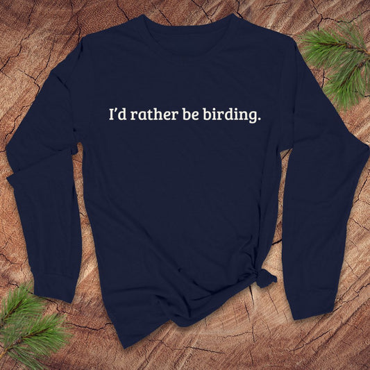 Navy blue long sleeve shirt with 'I'd rather be birding.' text on a wooden surface with pine branches.