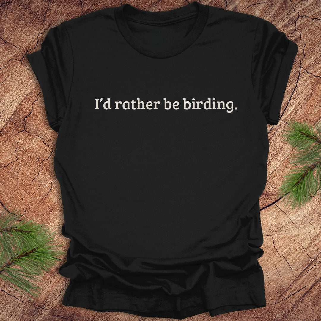 Black t-shirt with 'I'd rather be birding.' text on a wooden surface with pine branches.