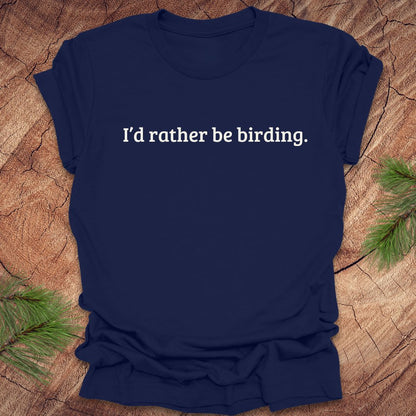 Navy blue t-shirt with 'I'd rather be birding.' text on a wooden surface with greenery.
