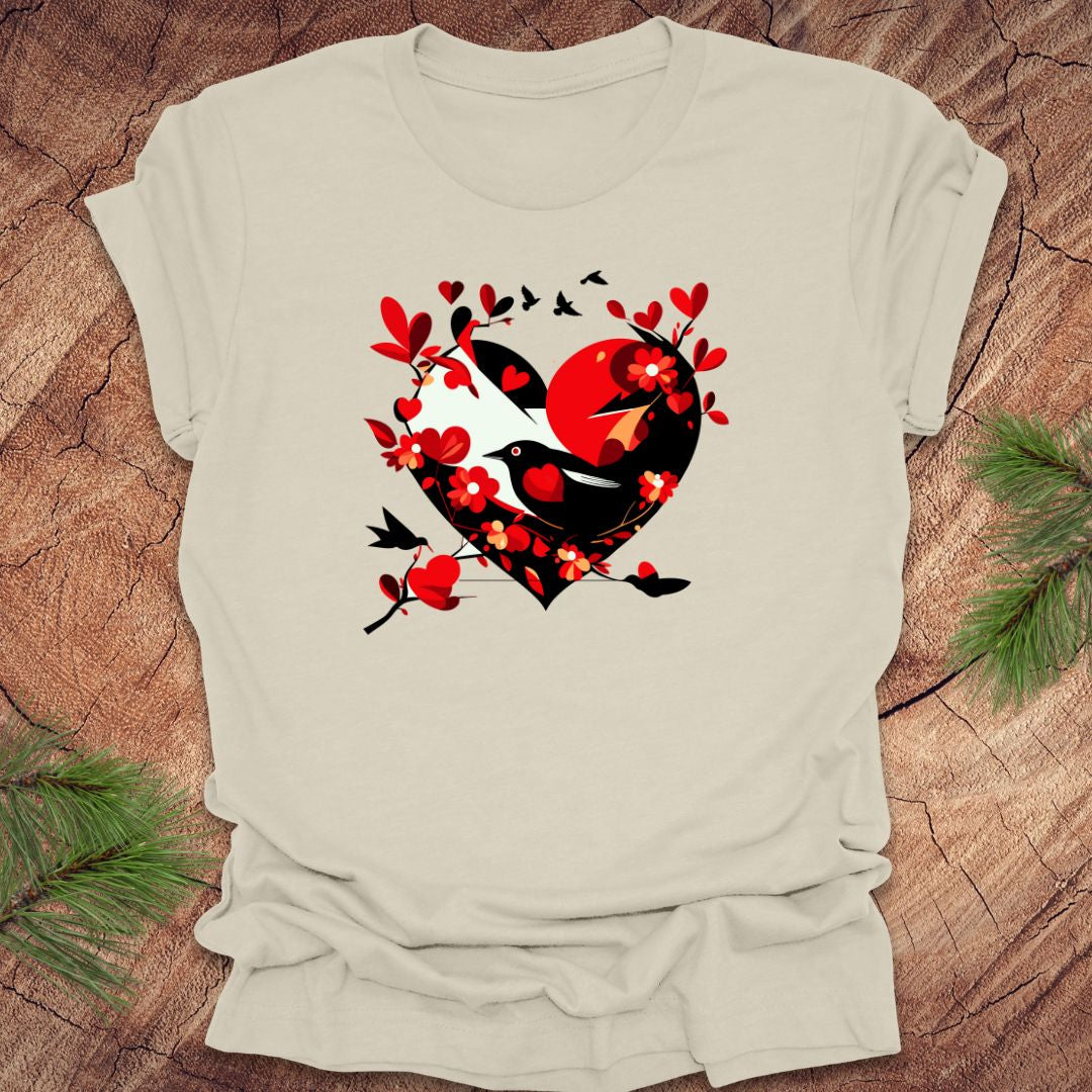 Beige t-shirt with a red and black heart with a raven inside of it, with red hearts flying off of it, on a wooden background.