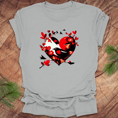 Silver t-shirt with a red and black heart with a raven inside of it, with red hearts flying off of it, on a wooden background.