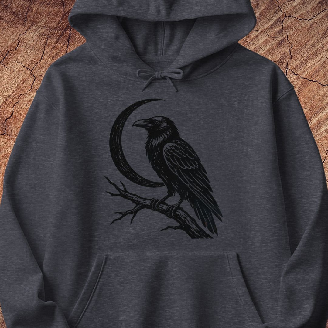A dark heather gray hoodie featuring a black graphic print of a raven perched on a branch in front of a crescent moon, displayed against a rustic wood background.