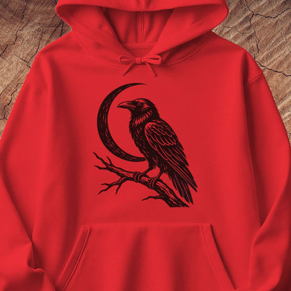 A bright red pullover hoodie with a black graphic of a raven perched on a branch in front of a crescent moon, displayed on a textured wood background.