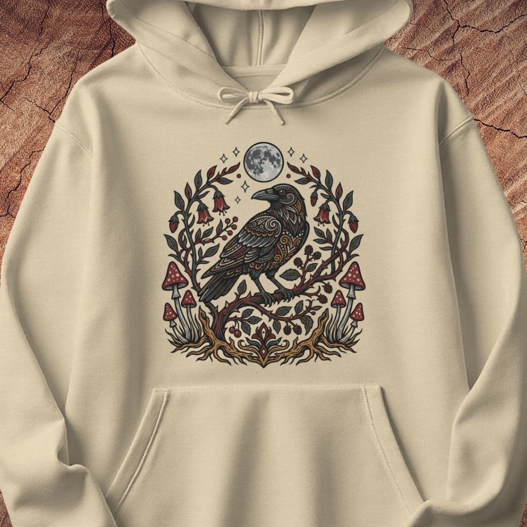 An off-white hooded sweatshirt with a detailed graphic of a black raven perched on a branch surrounded by red mushrooms and green leaves under a full moon, displayed on a textured brown wood background.