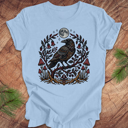 Baby blue t-shirt with a raven and nature-themed design on a wooden surface.