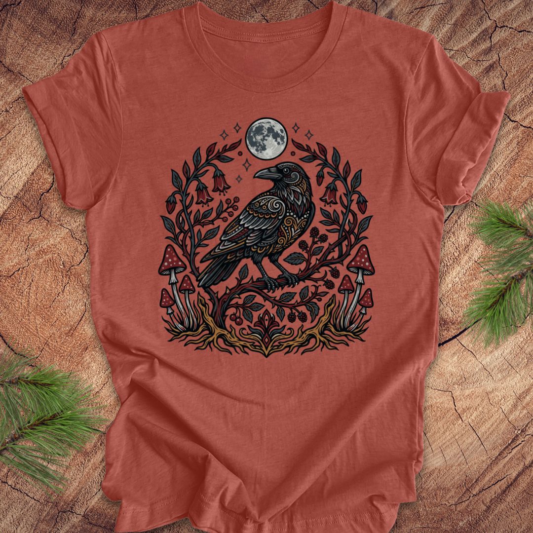Clay colored t-shirt with a raven and nature-themed design on a wooden surface.